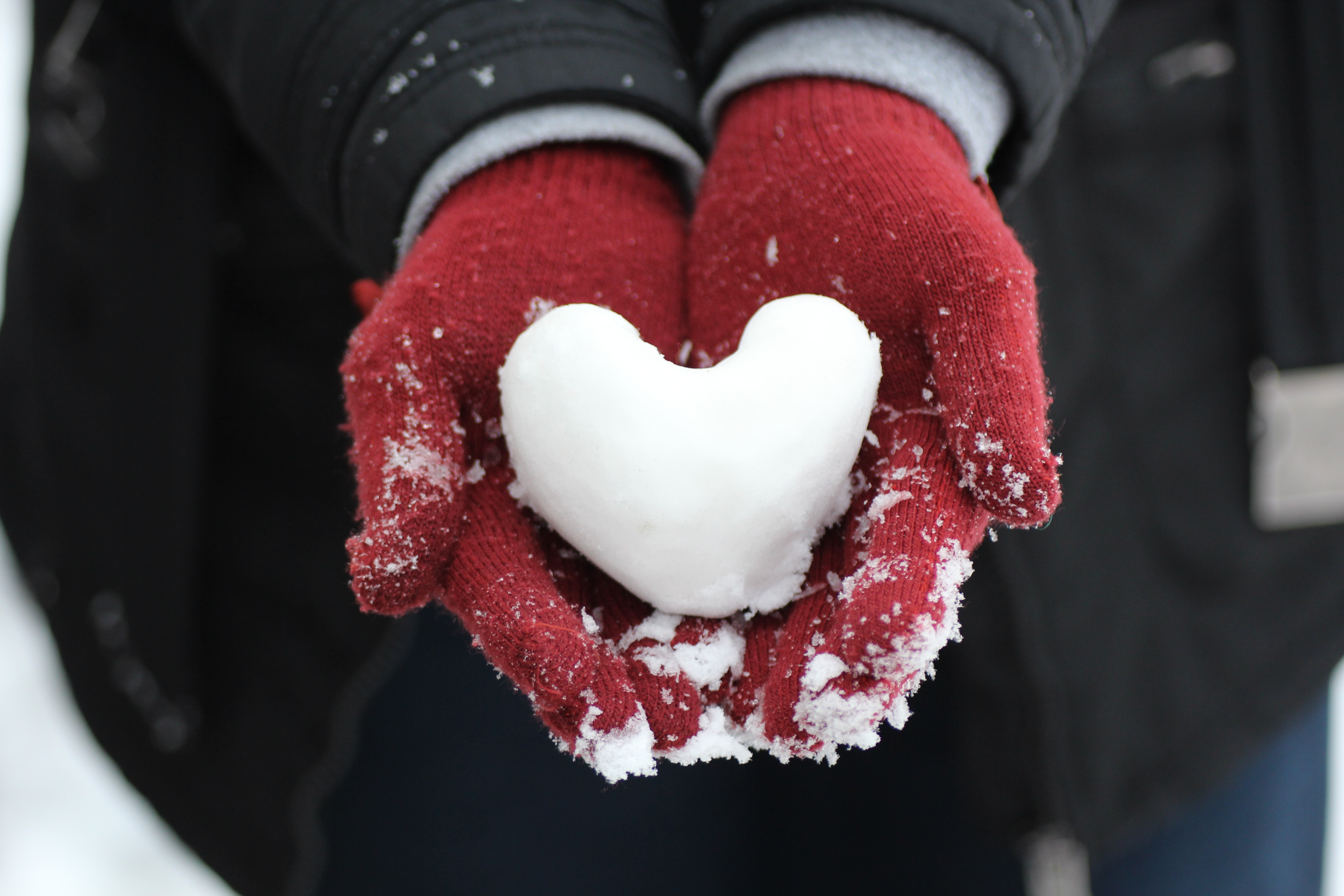gloved hands holding a heart made of snow